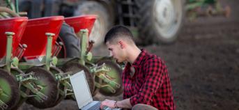 persoon met laptop langs tractor